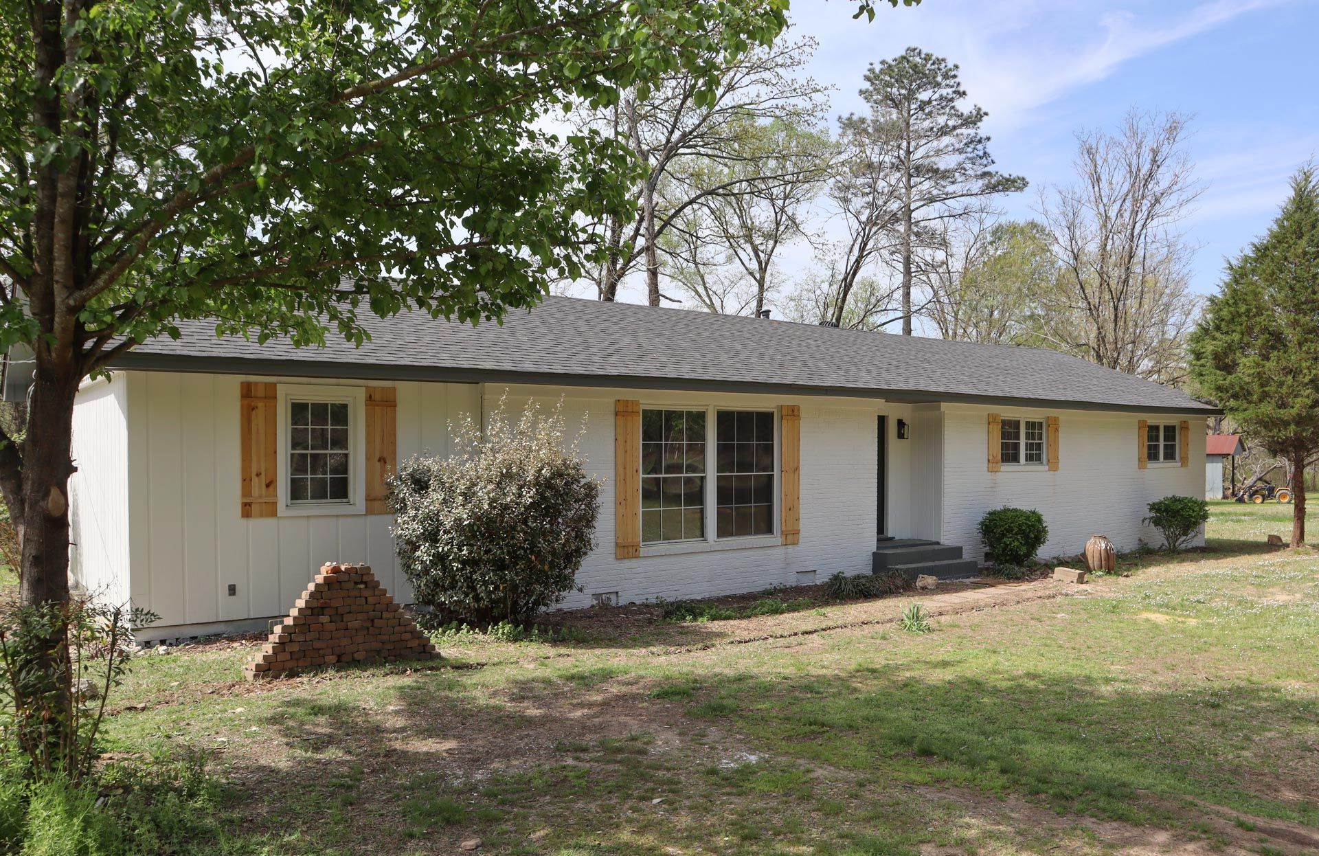 White-painted ranch house with wooden shutters, set in a grassy yard under a blue sky.