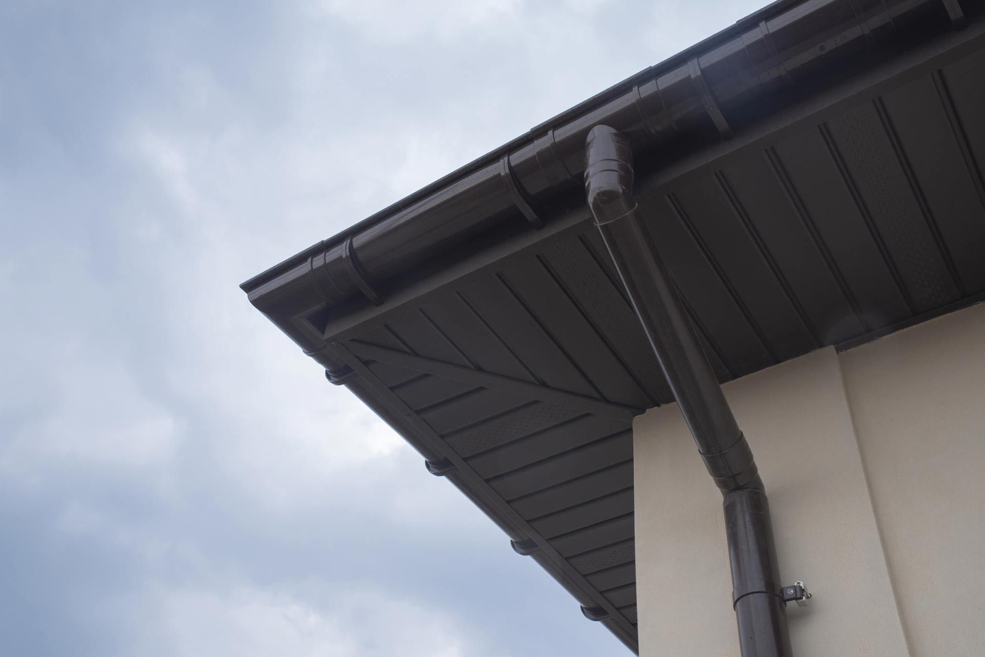 A close up of the roof of a house with a gutter and sky in the background.