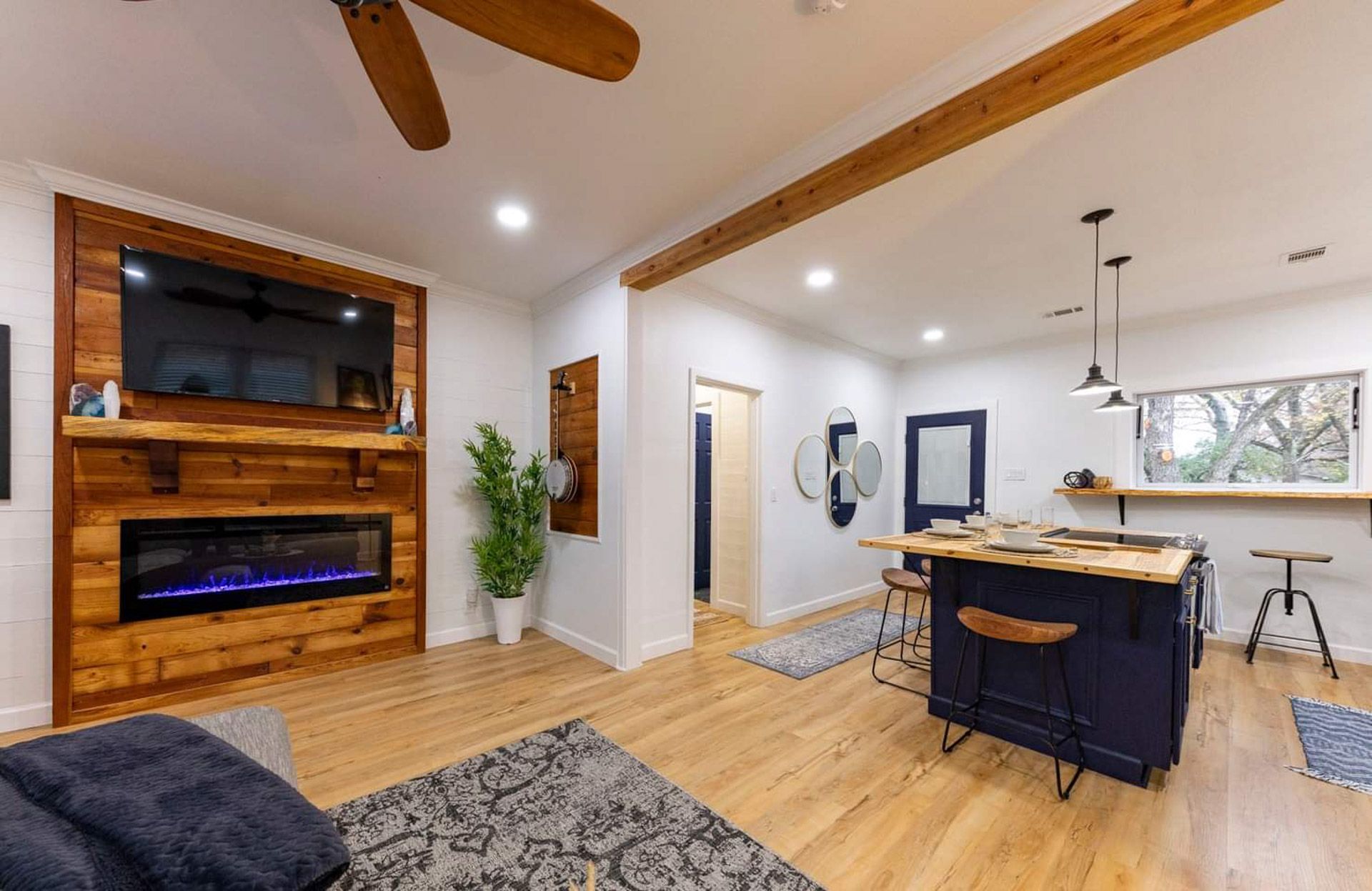 Modern open-concept living and dining room with wood ceiling beams, fireplace, and kitchen island