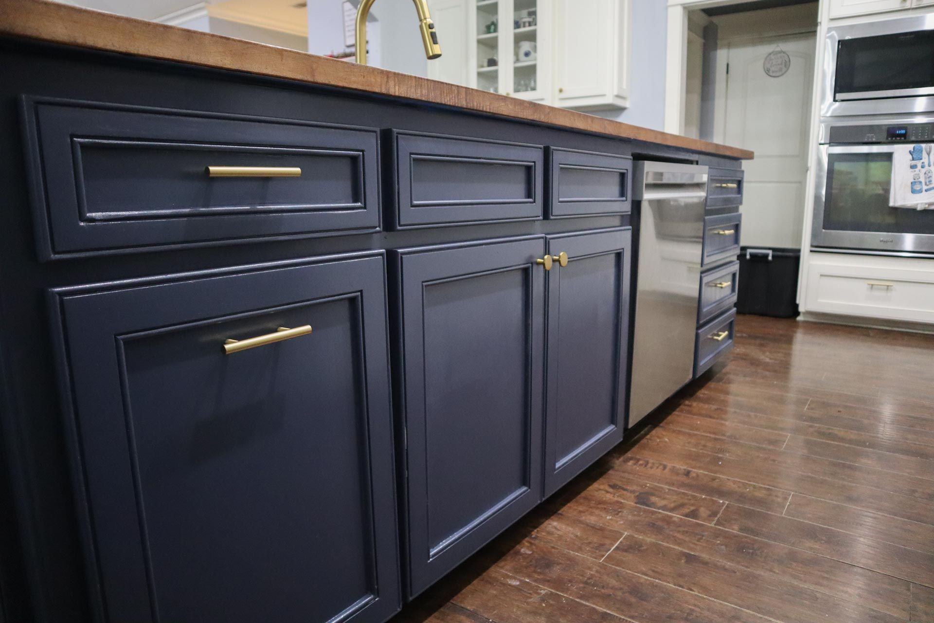 Dark blue kitchen island with wood countertop, gold hardware, and stainless steel dishwasher.