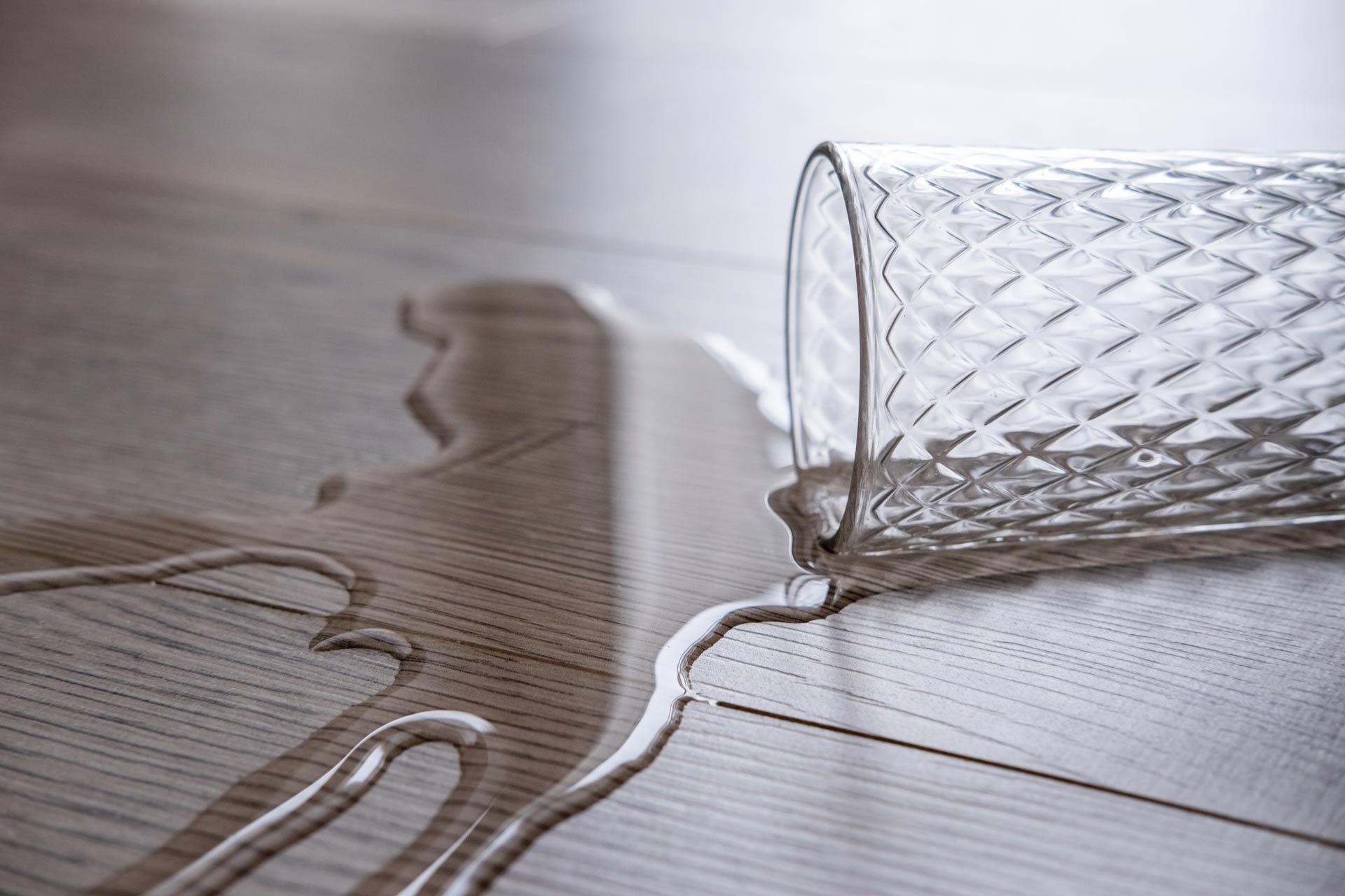 A glass of water spilled on a wooden floor.