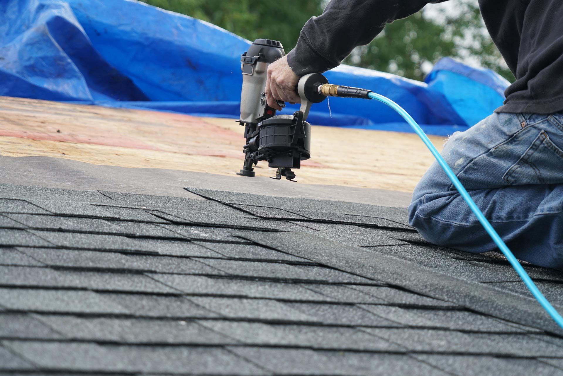 man using nail gun to install roof shingles