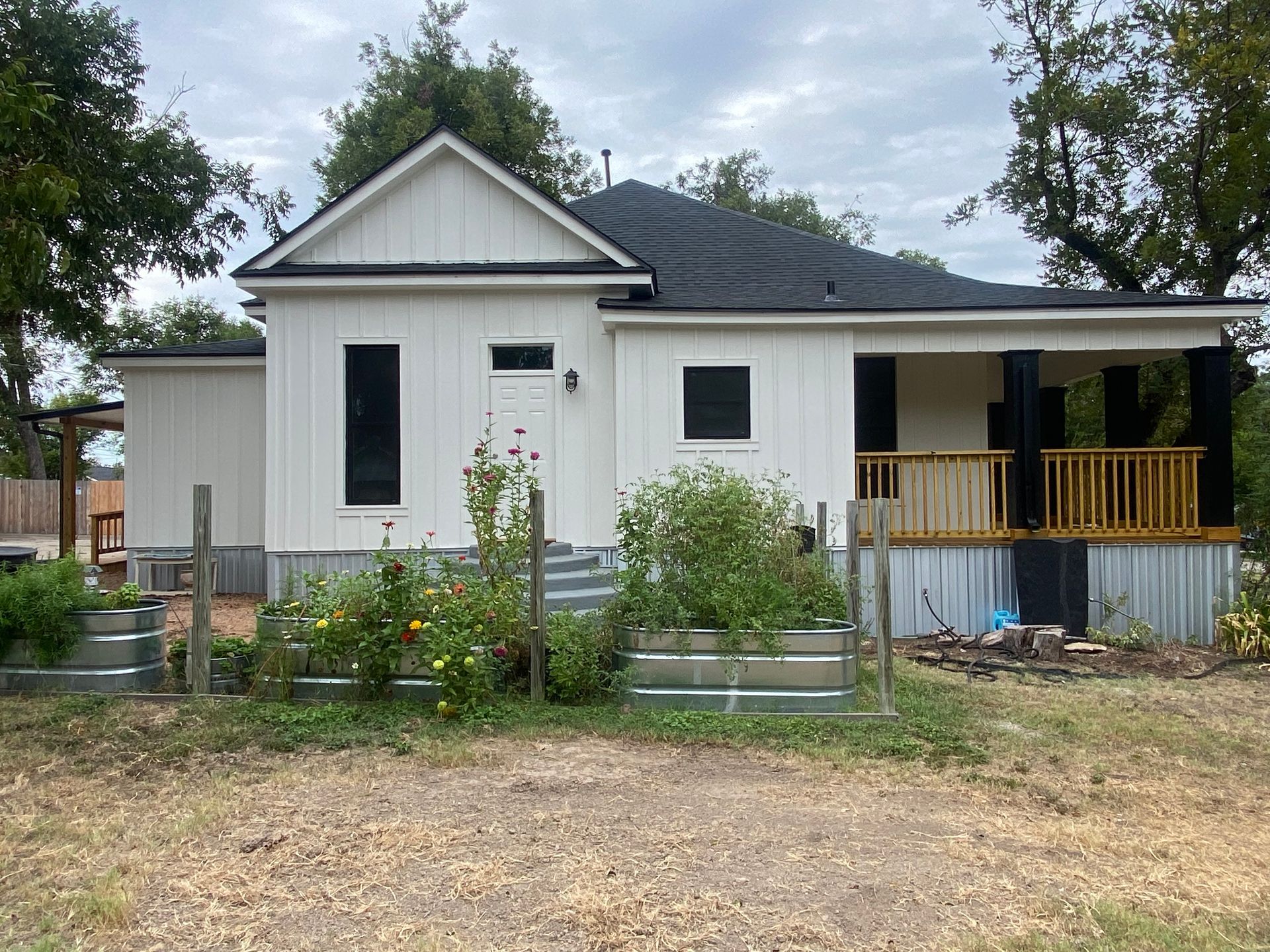 A white house with a black roof is sitting on top of a dirt field.