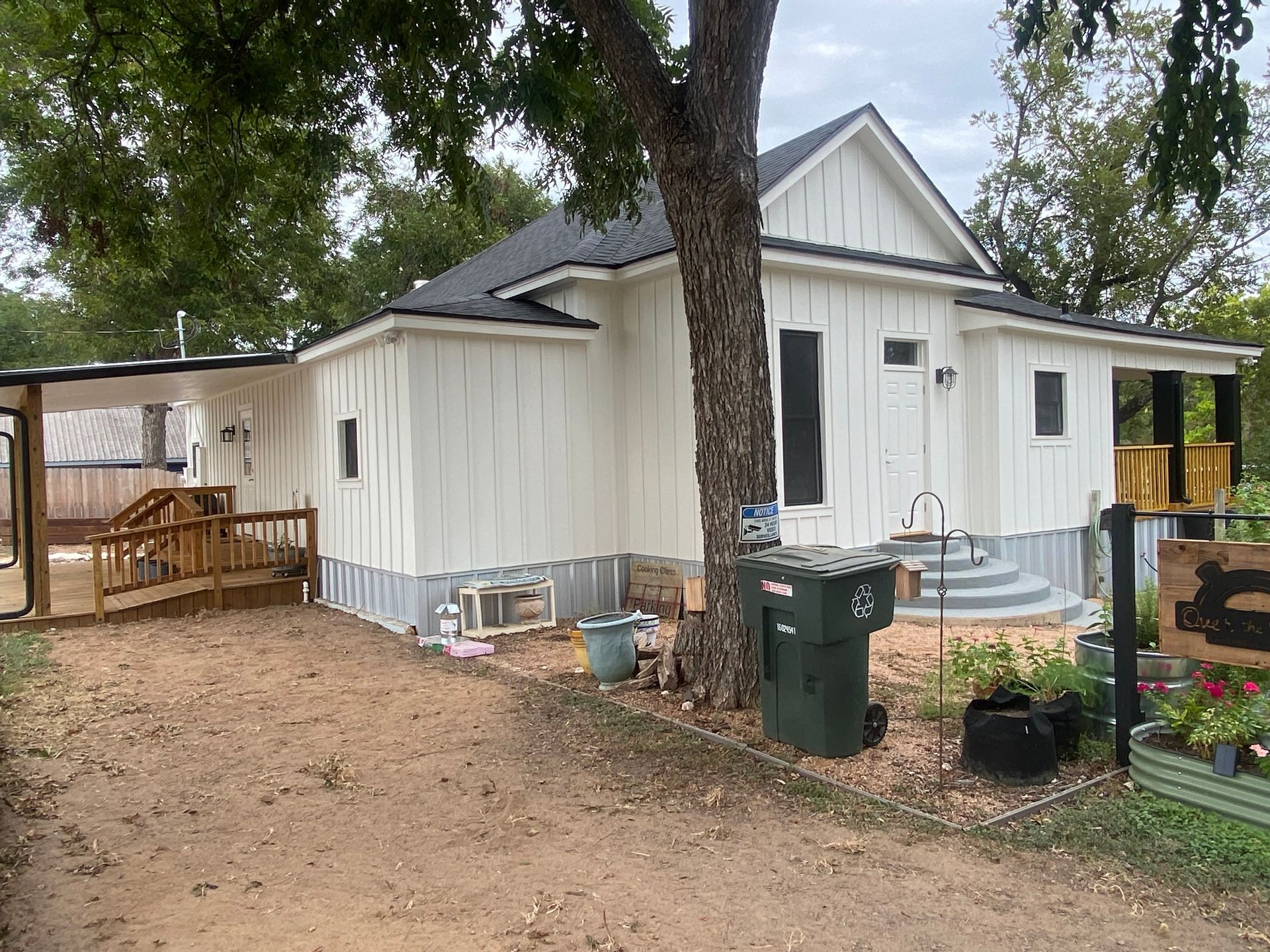 A white house with a black roof and a tree in front of it.