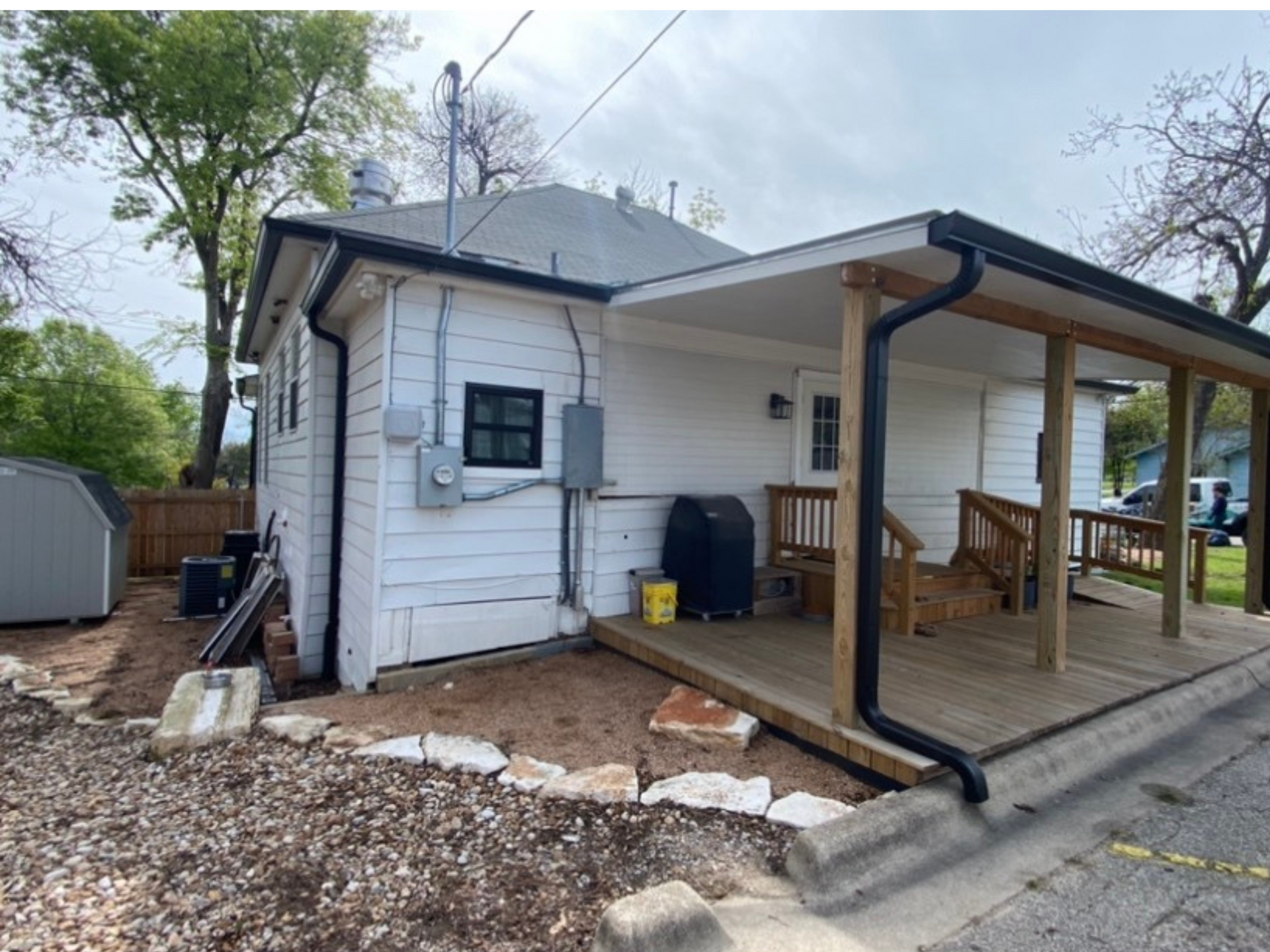 A white house with a porch and a shed in the backyard.