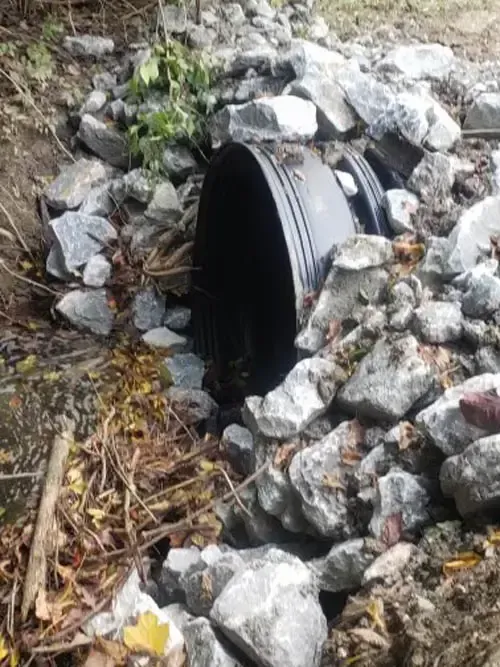 Black culvert pipe surrounded by rocks and debris.