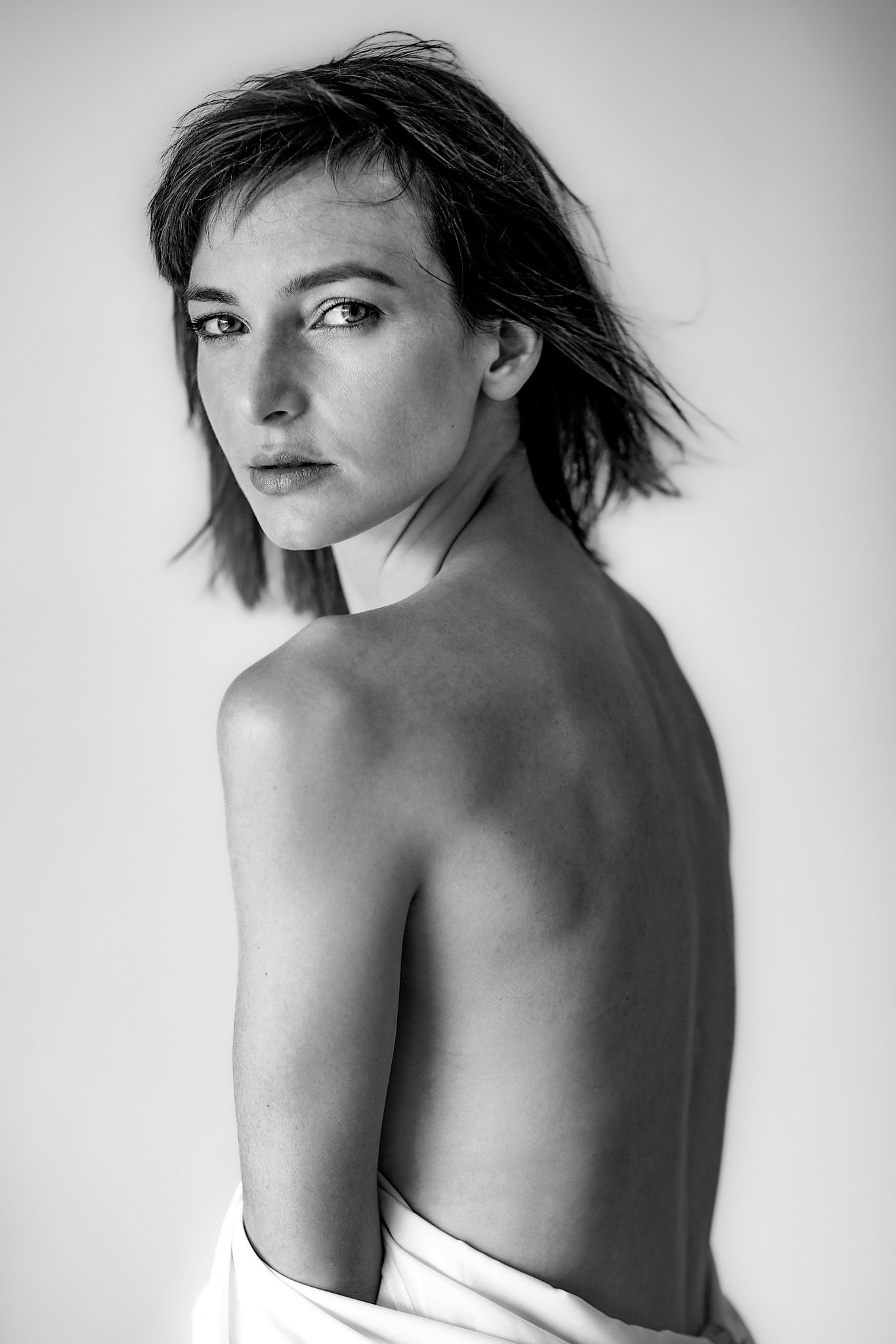 Woman looking over shoulder, partially nude, wearing a white sheet, in black and white.