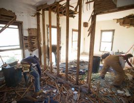 Construction workers demolishing a room, tearing down walls and debris scattered on the floor.