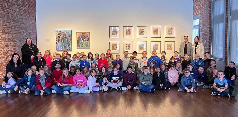 A group of students and teachers in an art gallery, posing in front of displayed art.