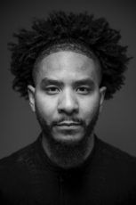 A black and white photo of a man with curly hair and a beard.