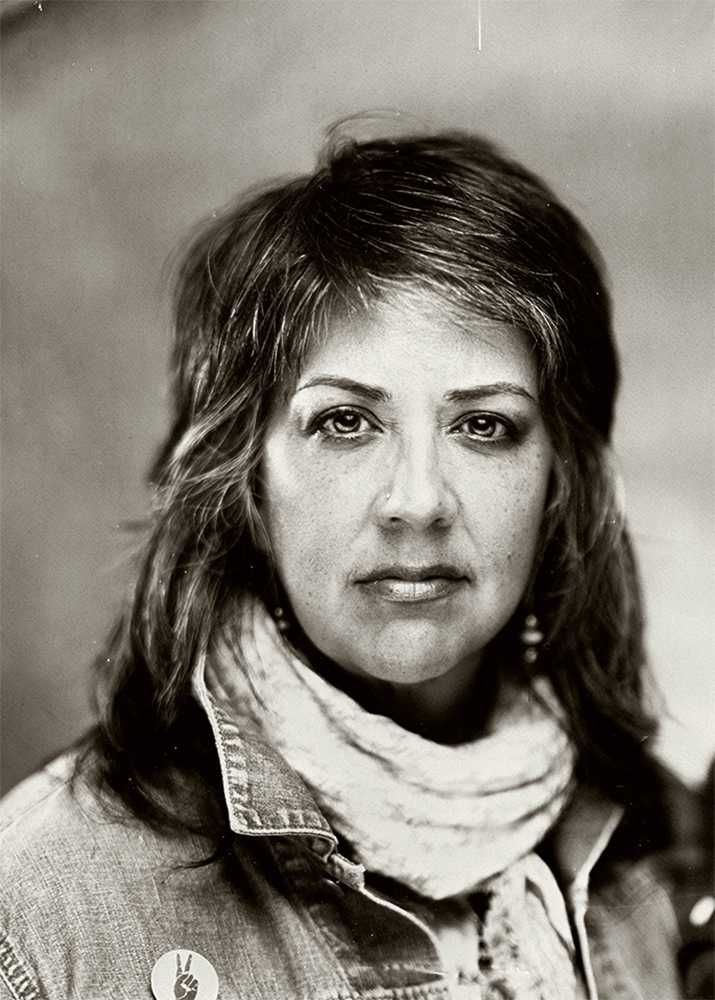 Woman with long hair, wearing a denim jacket and scarf, looking directly at the camera.
