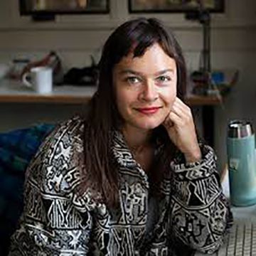 A woman is sitting at a desk with her hand on her chin.
