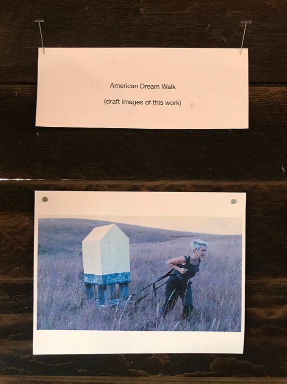 Person pulling a white, box-shaped structure through tall grass. Title: