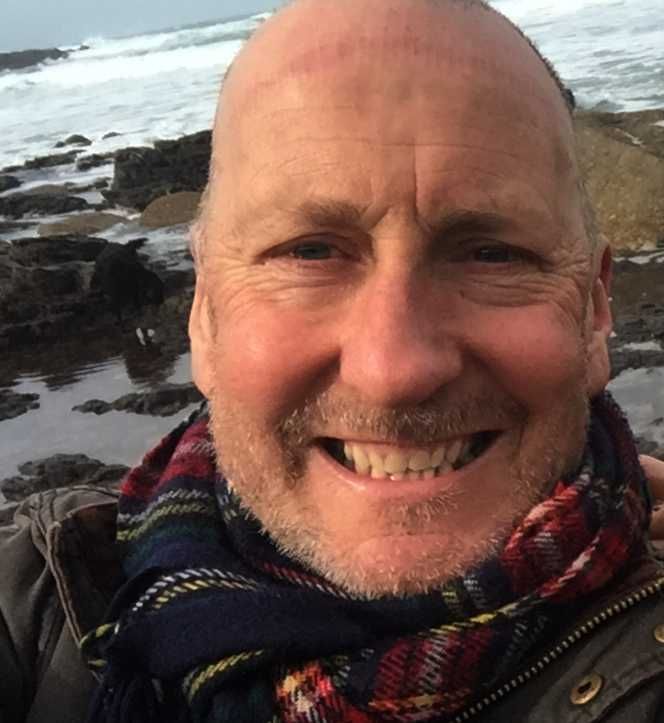 A bald man with a scarf around his neck is smiling for the camera.