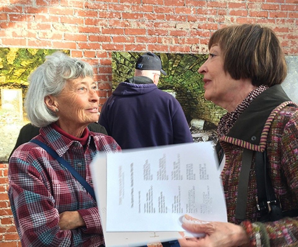 Two women are standing next to each other and one is holding a piece of paper with numbers on it