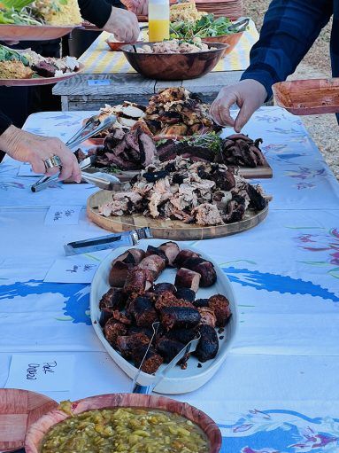 People serving themselves at a buffet-style outdoor meal with meat dishes, salads, and sides.