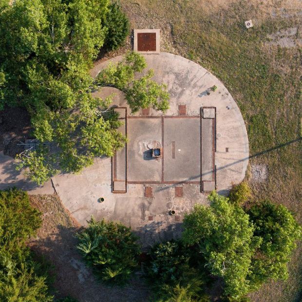 Aerial view of a circular concrete structure with a rectangular center, surrounded by grass and trees.
