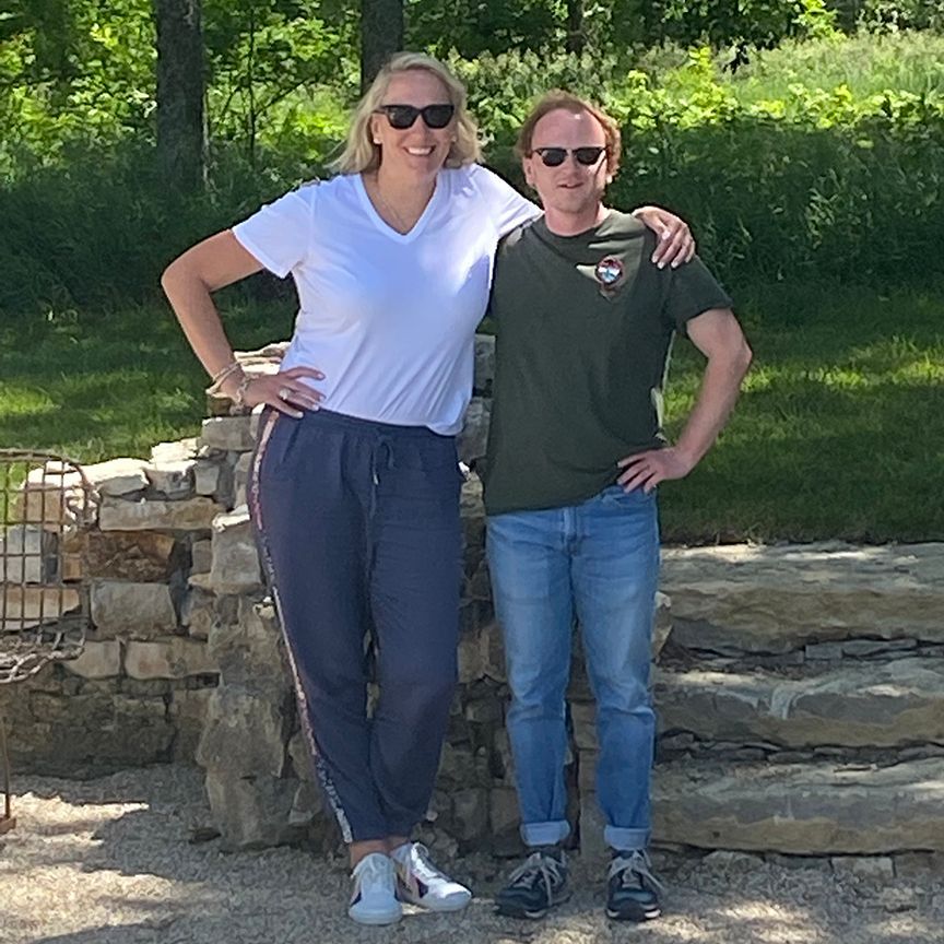 Woman in white shirt and man in green shirt pose together outdoors.