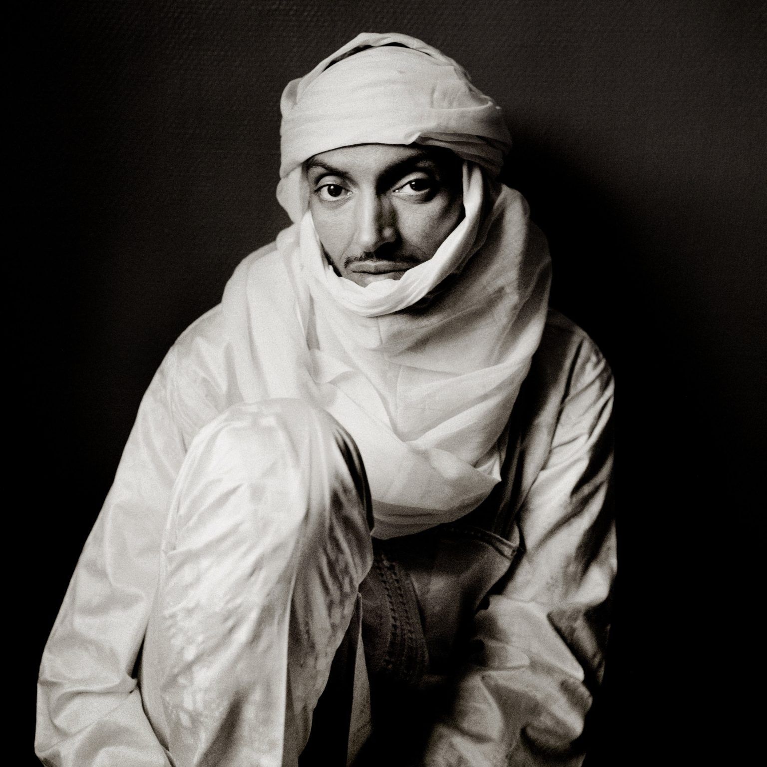 Man wearing white turban and robes, looking directly at the camera, in black and white.