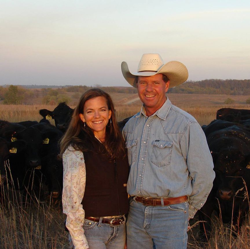 A man in a cowboy hat stands next to a woman in a field of cows