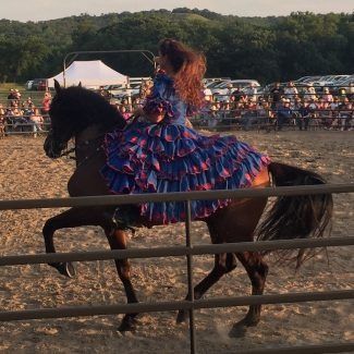 A girl in a blue and red dress is riding a horse behind a fence.