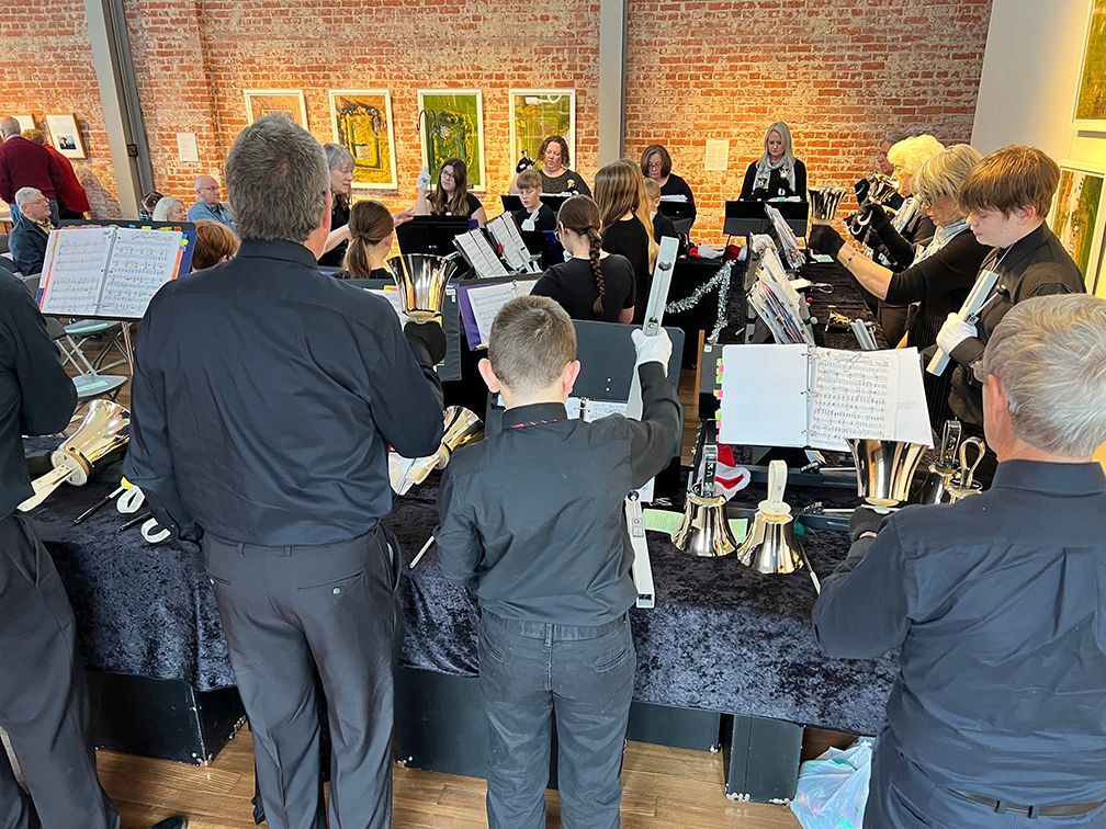 Adults and children play the bells in a performance of Christmas music