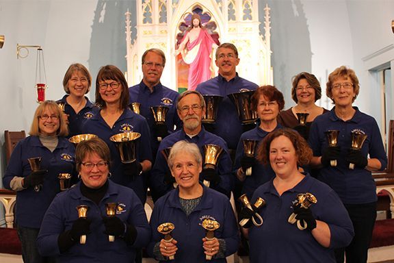 A group of people holding bells in front of a statue of jesus