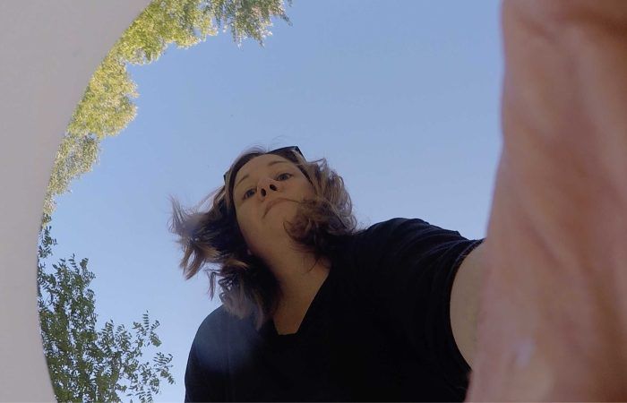 Woman looking down, from a low angle, with a blue sky visible above.