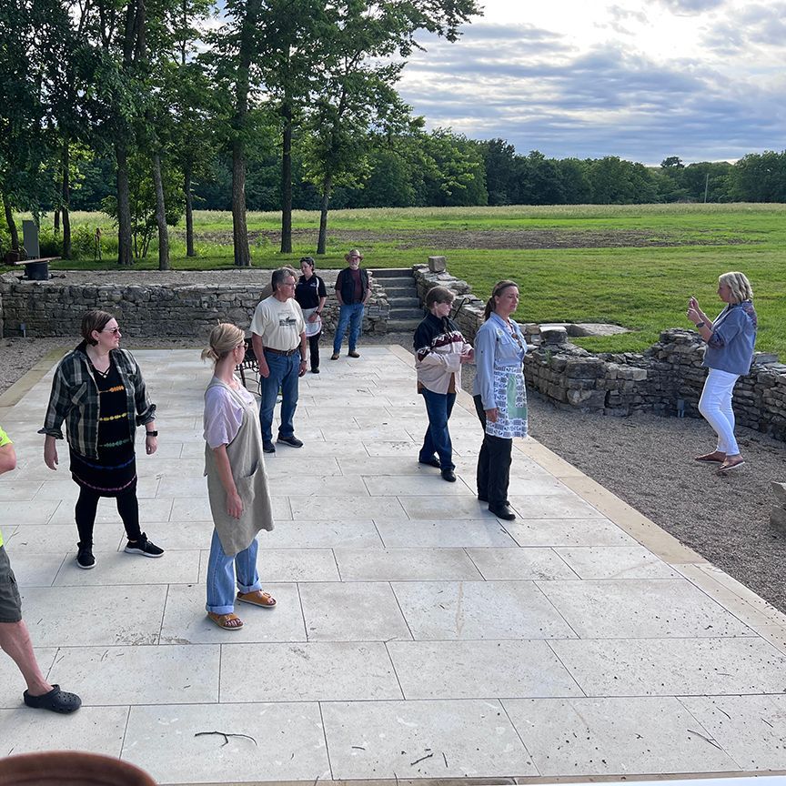 A group of people standing outside, listening to a woman. They appear to be on a tour of an old ruin.