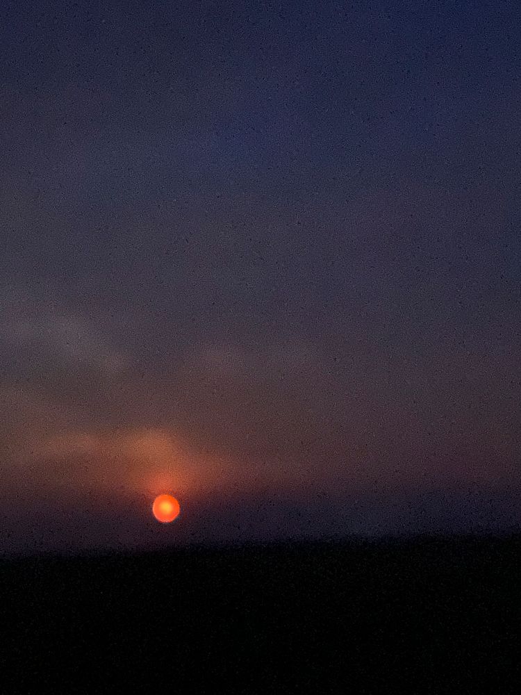 The sun is setting in the night sky over a field.