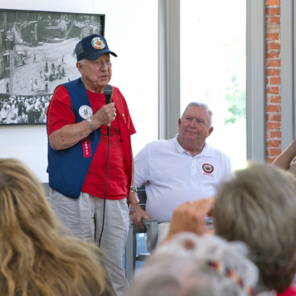 A man in a red shirt is speaking into a microphone