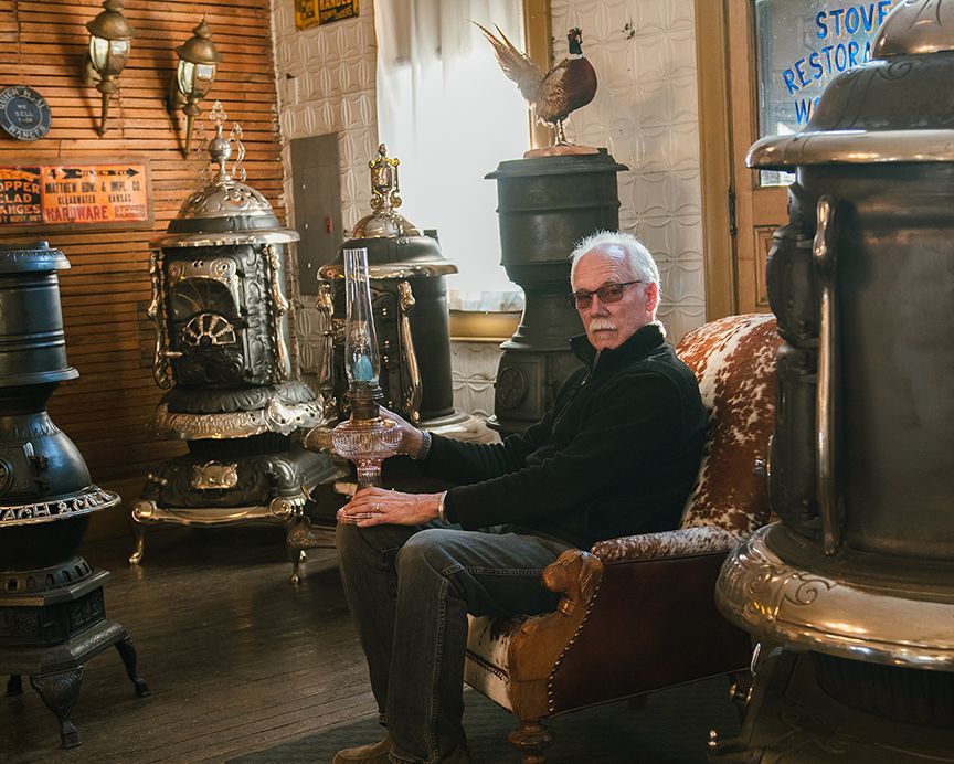 A man is sitting in a chair in a room with a lot of antique stoves.