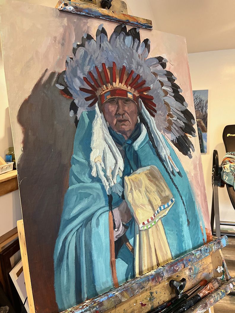 Oil painting of Native American elder in headdress and blue robe, painting on easel in studio.
