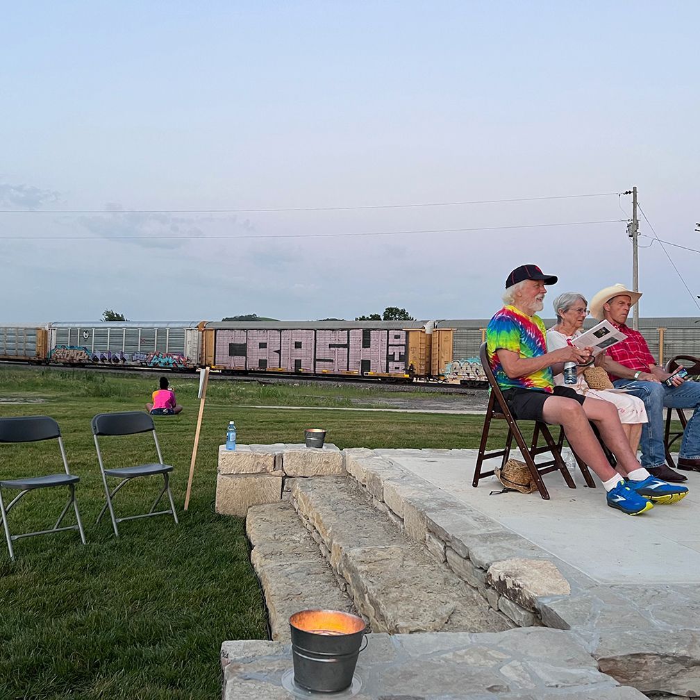 People seated outdoors, reading with train car graffitied