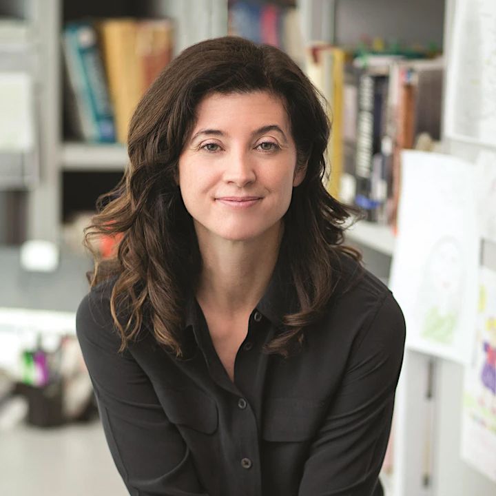 Woman with long brown hair smiles, wearing a black shirt, in a home office.