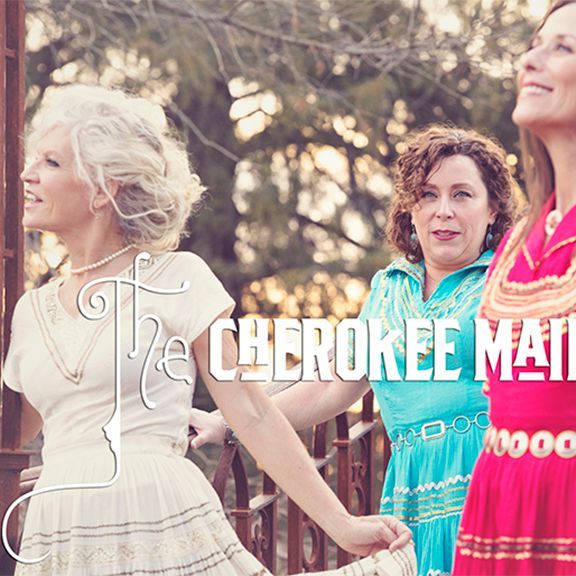 Three women in colorful dresses, posing outdoors, The Cherokee Maidens band.