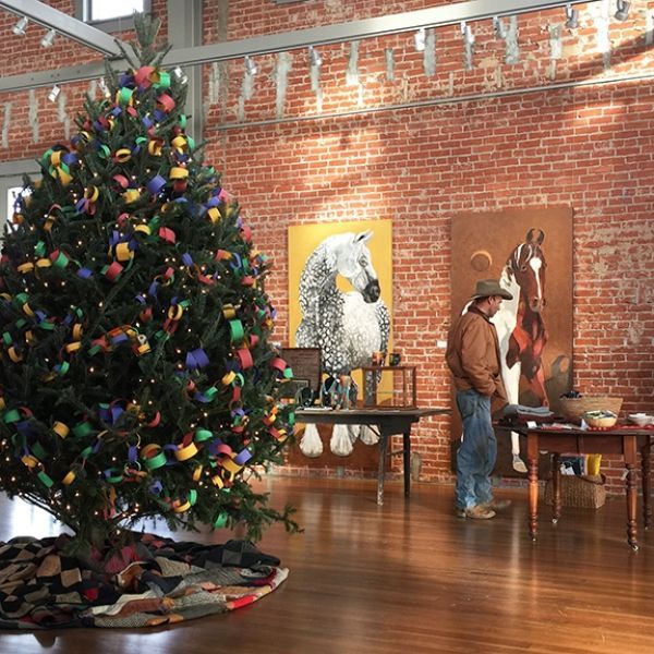 A man stands in front of a painting of a horse and a christmas tree