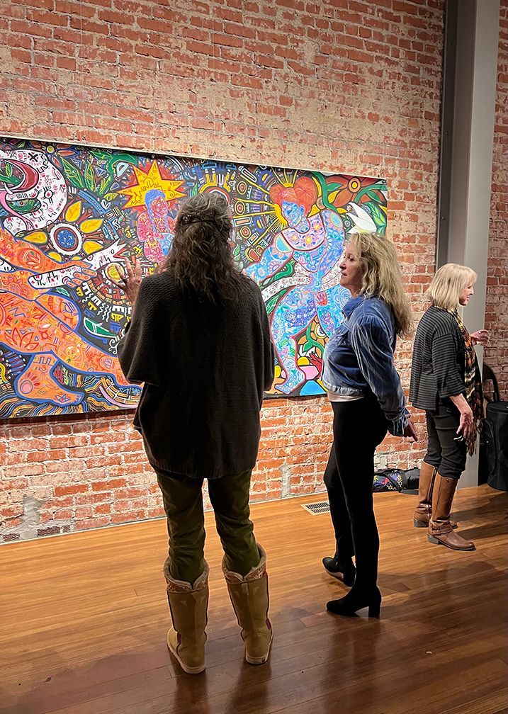 People viewing a colorful mural in an art gallery. Brick wall backdrop, wood floor.