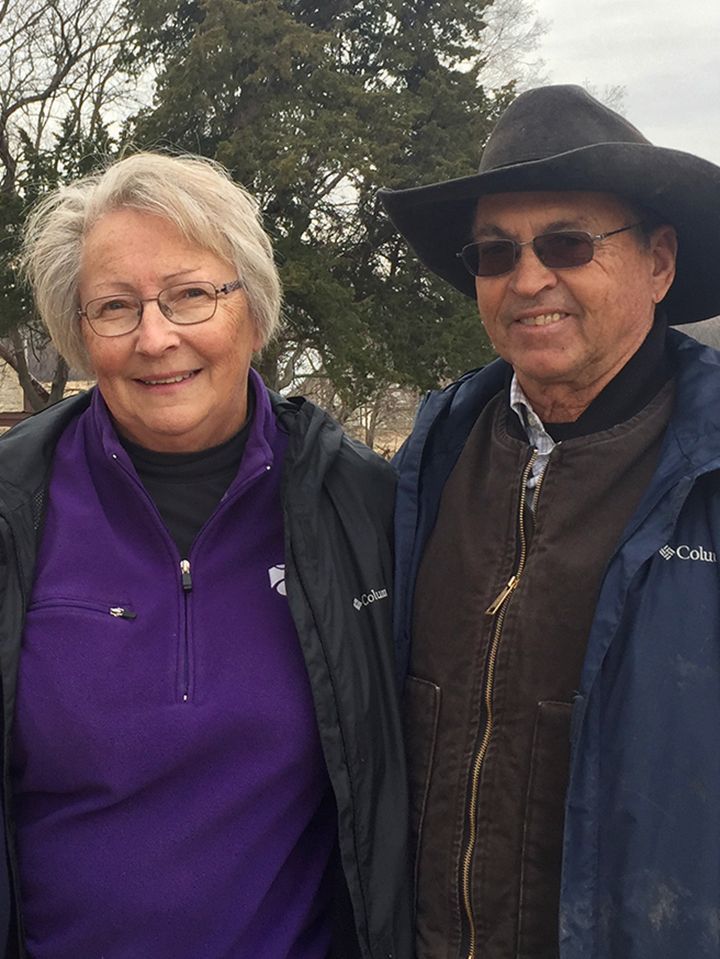 A man and a woman are posing for a picture and the woman is wearing a purple jacket.