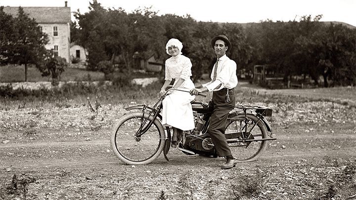 A man and a woman are riding a motorcycle on a dirt road.