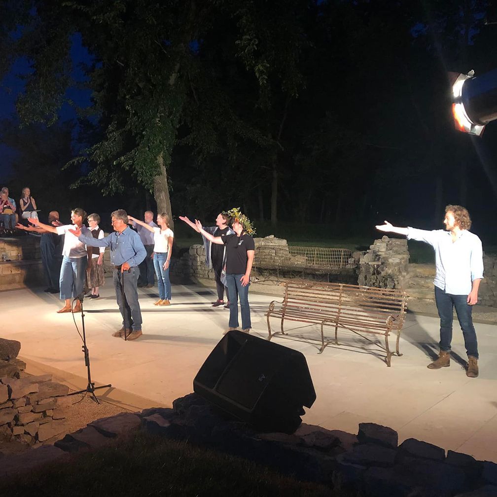 A group of people are on stage, some with arms outstretched, during a night performance.
