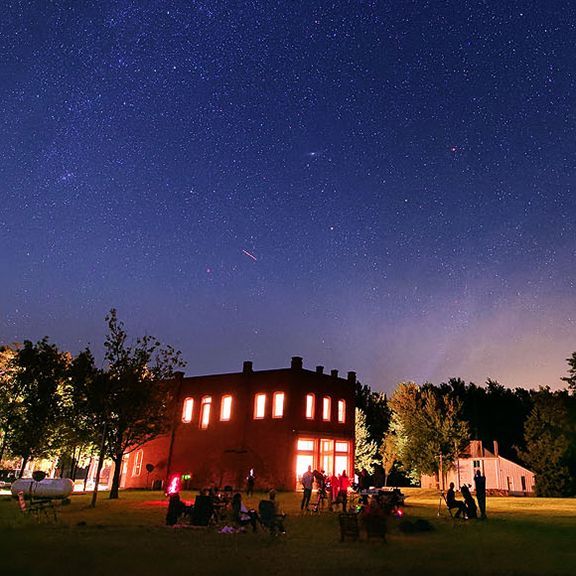 A group of people are gathered in front of a building at night under a starry sky.
