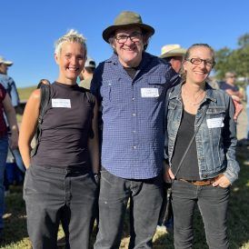 Three people smiling outdoors, man in hat between two women.