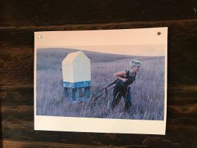 Woman pulling a house-shaped structure across a field. The structure is white and blue.