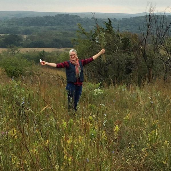 A woman is standing in a field with her arms outstretched.