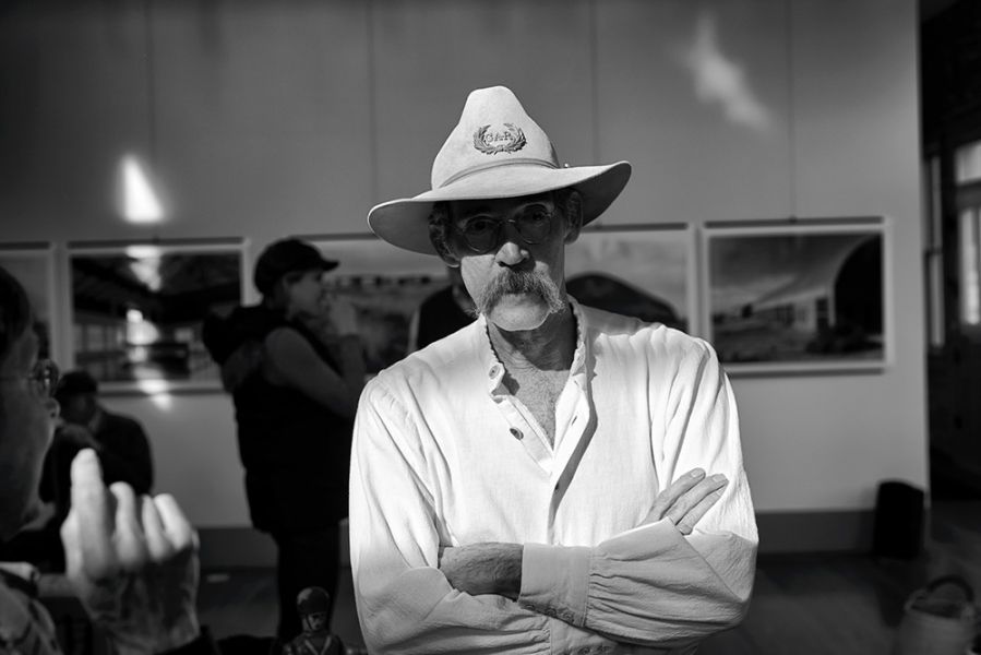 A man wearing a cowboy hat and sunglasses is standing with his arms crossed.