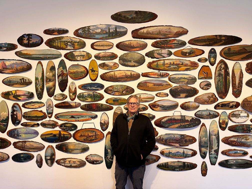 close up of 3 colorful log slab paintings of landscapes: pine trees, lake, a cabin, and sunset