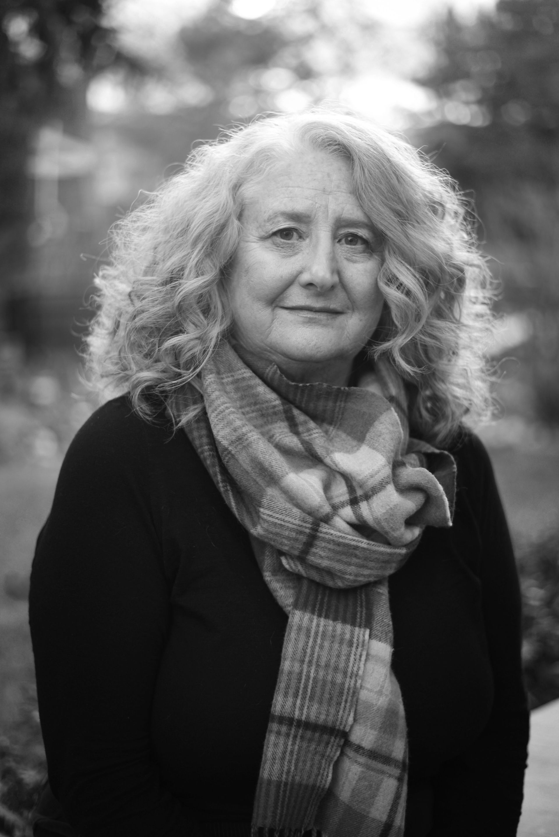 Woman with curly grey hair wearing a scarf, looking at the camera, outdoors.