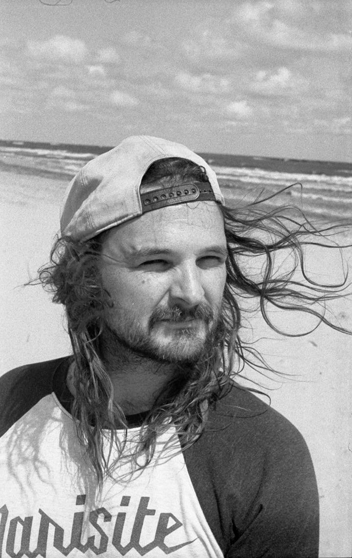 A man with long hair is wearing a baseball cap and a shirt that says marisite.