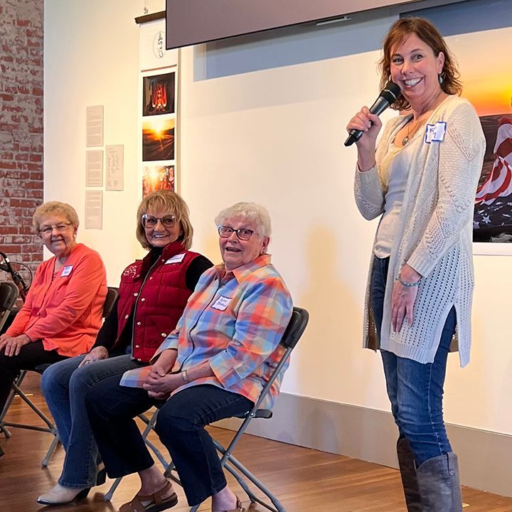 Woman speaks into microphone at a panel discussion with three seated women.